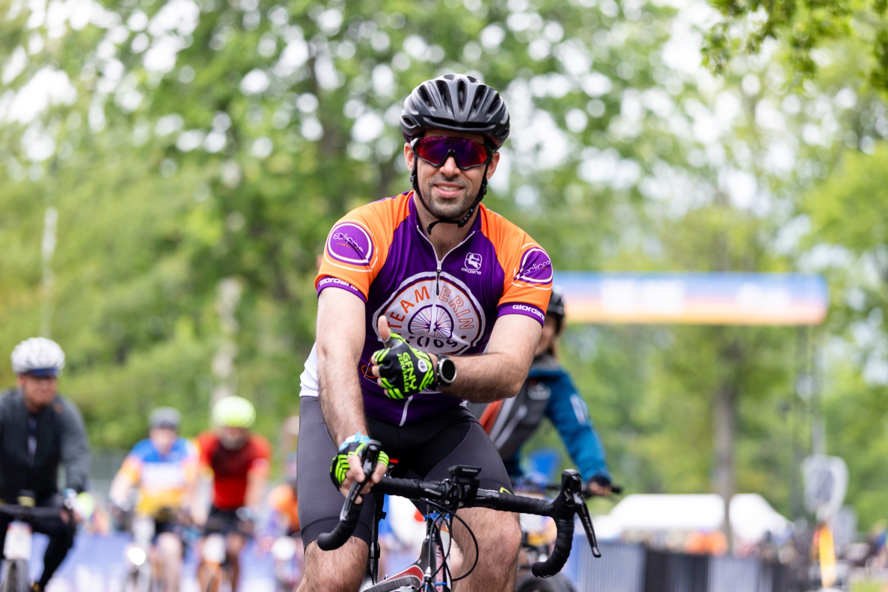 A smiling Team Erin cyclist in orange and purple gives a thumbs-up